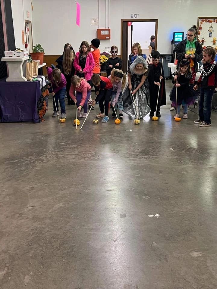 Children in Halloween costumes playing a pumpkin rolling game