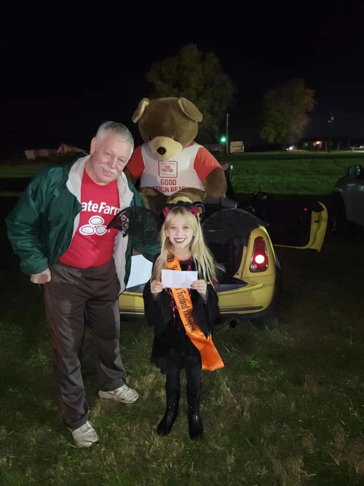 A smiling man and a girl in Halloween costume beside a Mini Cooper
